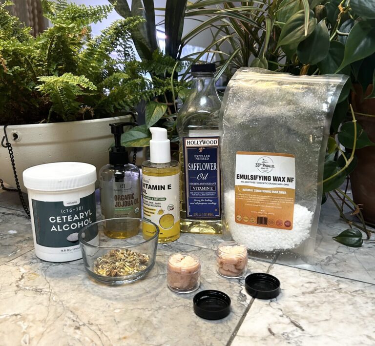 Ingredients for Emma's Garden Scub sit on a counter surrounded by green plants.