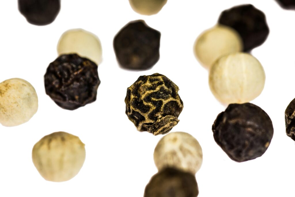 Dried black and white peppercorns float over a white back ground